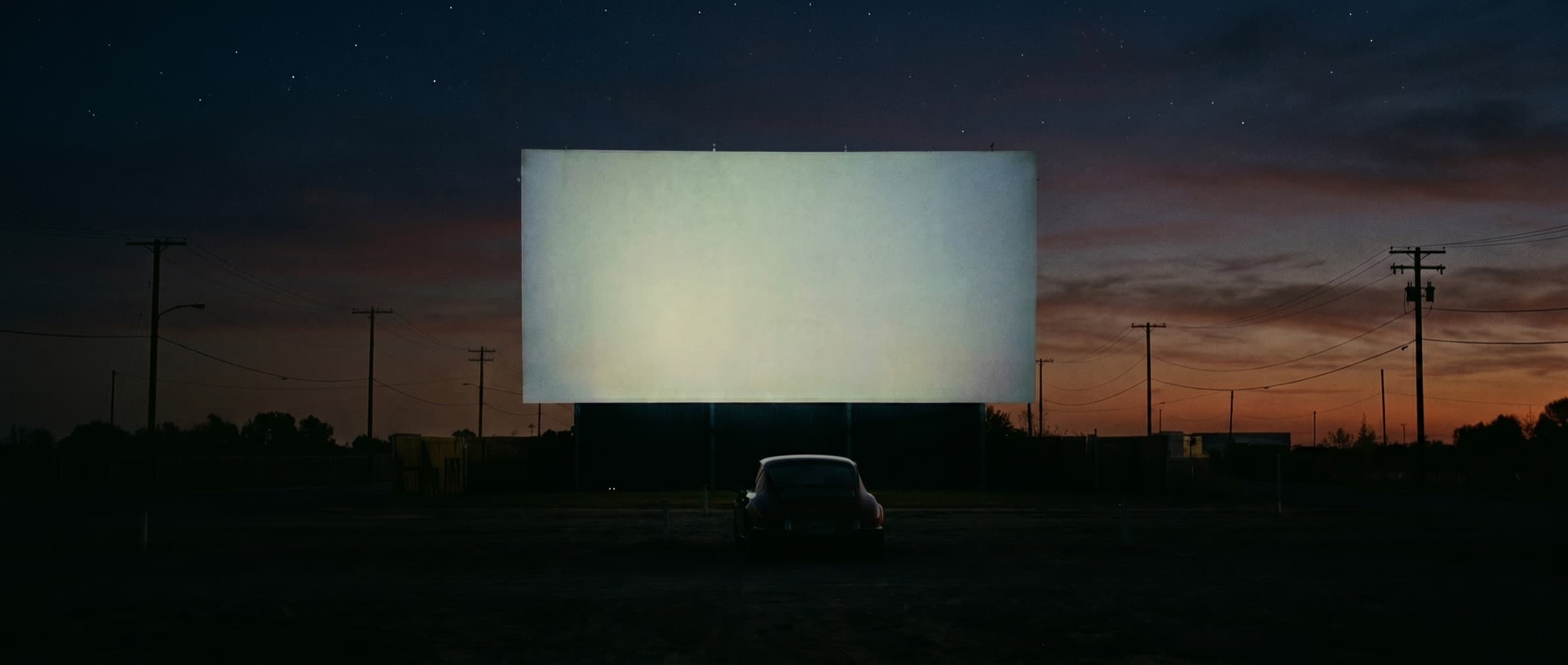 A classic Porsche 911 alone at a hazy drive-in theater at dusk